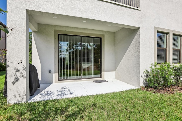 view of exterior entry featuring a patio area and a lawn