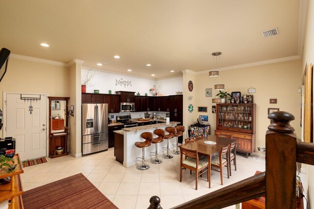 kitchen with light tile patterned floors, hanging light fixtures, stainless steel appliances, a kitchen breakfast bar, and light stone countertops