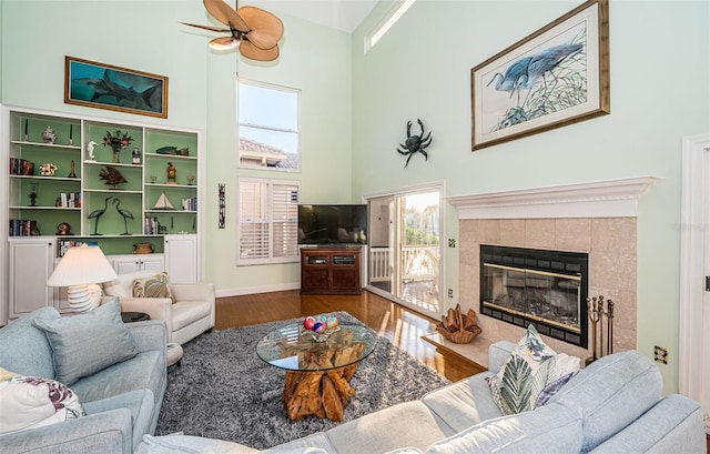 living room with a tiled fireplace, hardwood / wood-style flooring, ceiling fan, and a towering ceiling