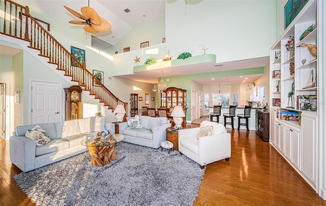 living room featuring ceiling fan with notable chandelier, a towering ceiling, and hardwood / wood-style floors