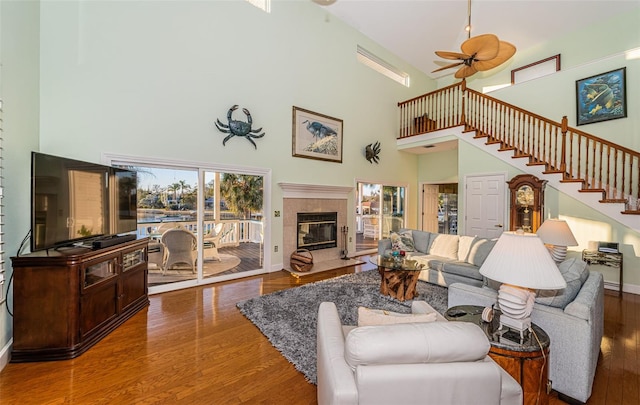 living room with a tiled fireplace, hardwood / wood-style flooring, ceiling fan, and a towering ceiling