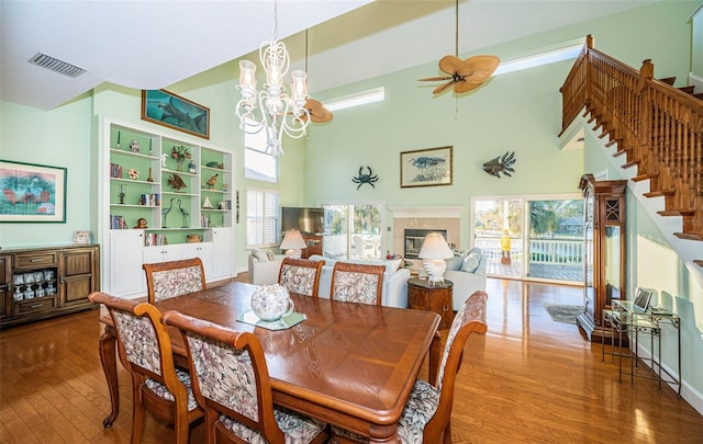 dining room with hardwood / wood-style flooring, ceiling fan with notable chandelier, and a towering ceiling