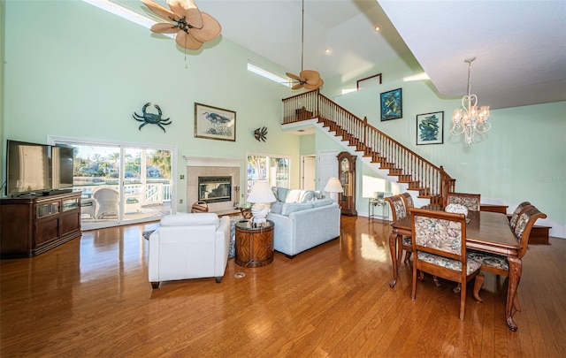 living room with ceiling fan with notable chandelier, a towering ceiling, hardwood / wood-style floors, and a tile fireplace