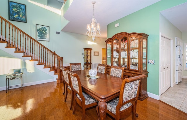 dining space featuring hardwood / wood-style flooring, a towering ceiling, and a chandelier