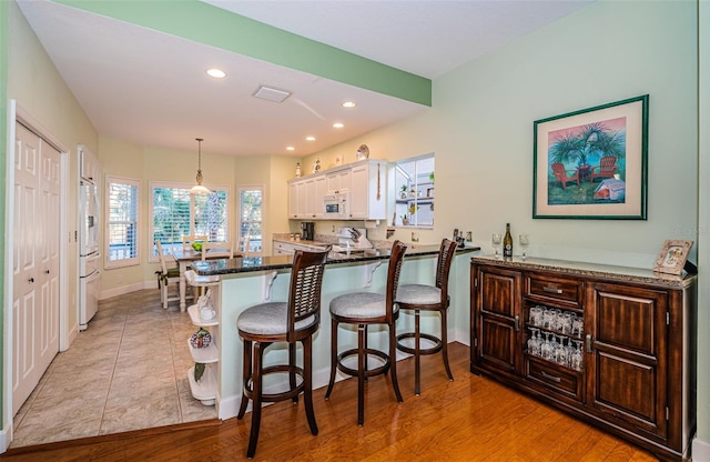 kitchen with white cabinetry, a kitchen bar, hanging light fixtures, kitchen peninsula, and white appliances