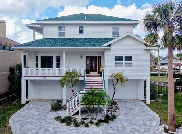 beach home featuring an attached garage, covered porch, a shingled roof, decorative driveway, and stairway