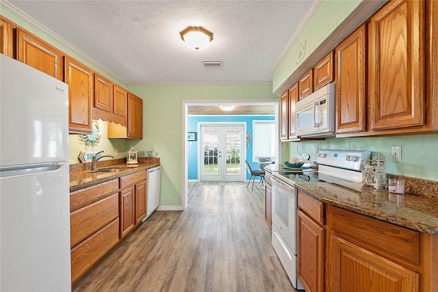 kitchen with sink, dark stone countertops, white appliances, light wood-type flooring, and french doors