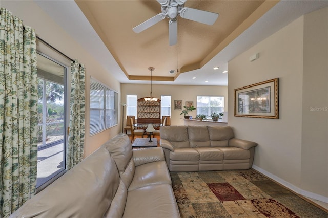 living room with ceiling fan with notable chandelier and a raised ceiling