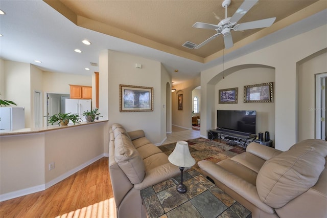 living room with ceiling fan, a raised ceiling, and light hardwood / wood-style floors