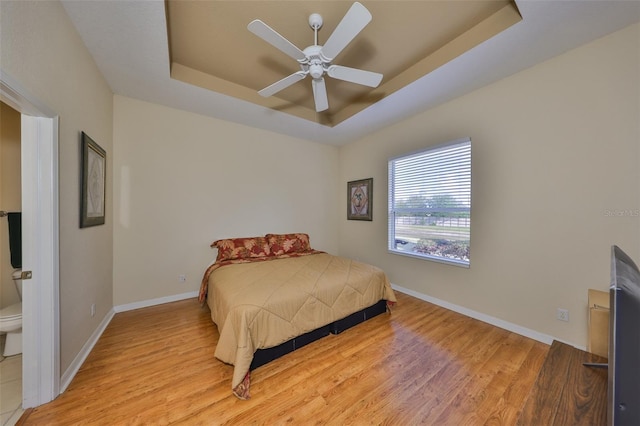 bedroom with a tray ceiling, light hardwood / wood-style floors, and ceiling fan