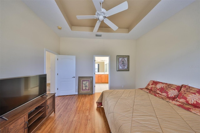 bedroom with a raised ceiling, ceiling fan, connected bathroom, and light hardwood / wood-style floors