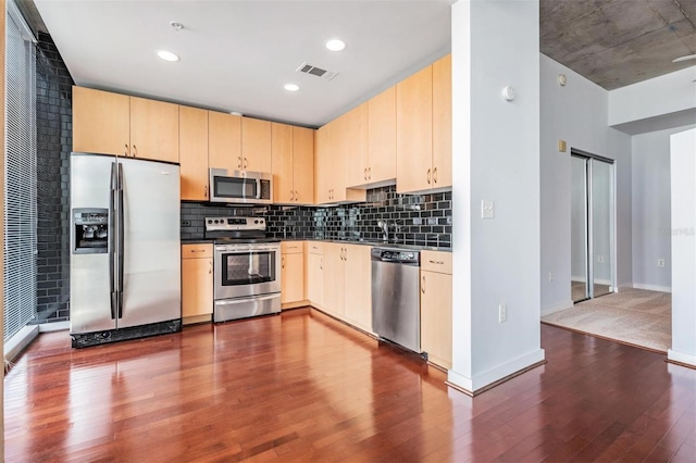 kitchen with a barn door, appliances with stainless steel finishes, hardwood / wood-style flooring, and light brown cabinets