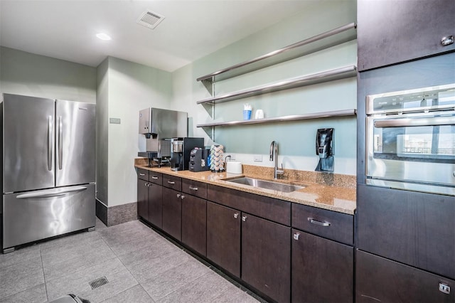 kitchen featuring sink, light tile patterned floors, dark brown cabinetry, stainless steel appliances, and light stone countertops