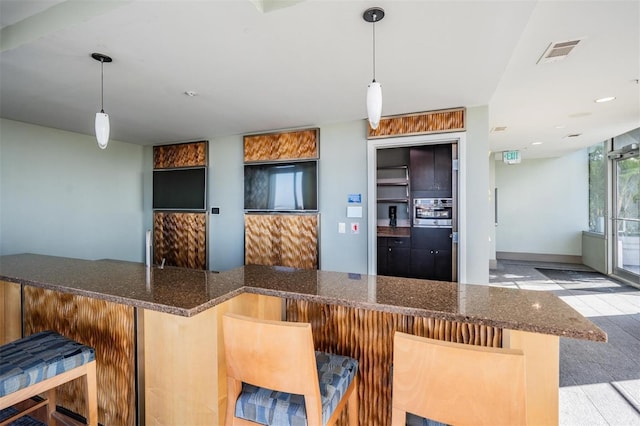 kitchen with hanging light fixtures, a breakfast bar area, dark stone counters, and kitchen peninsula