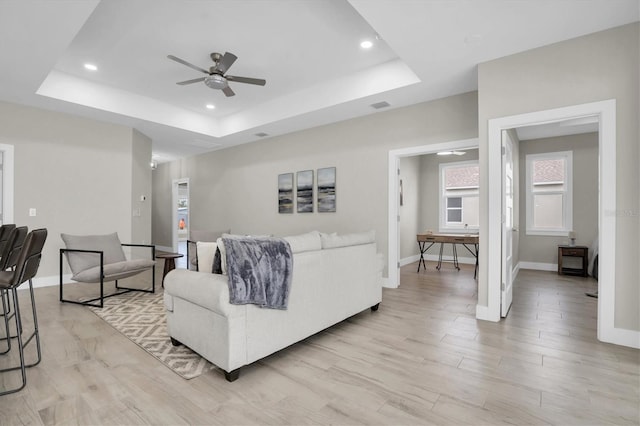 living room featuring ceiling fan, a raised ceiling, and light wood-type flooring