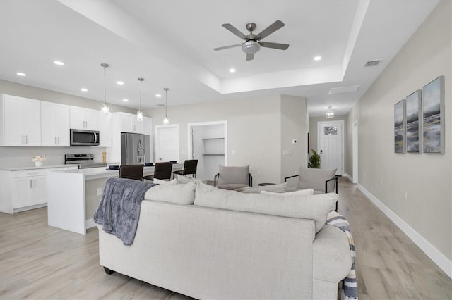 living room featuring a raised ceiling, ceiling fan, light hardwood / wood-style floors, and built in shelves