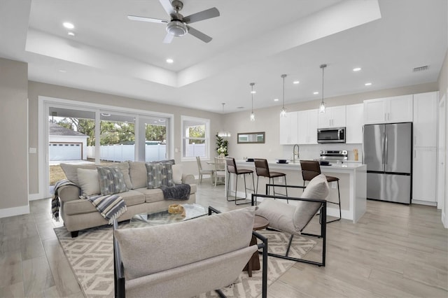 living room with ceiling fan, light hardwood / wood-style floors, and a tray ceiling