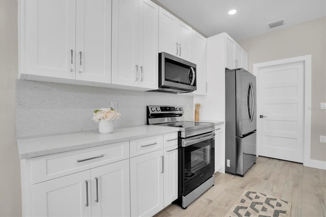 kitchen with backsplash, stainless steel appliances, light stone counters, light hardwood / wood-style floors, and white cabinets