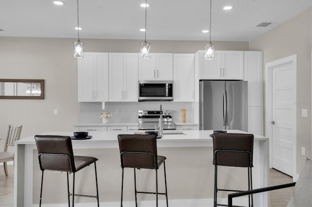 kitchen with sink, white cabinetry, hanging light fixtures, appliances with stainless steel finishes, and an island with sink