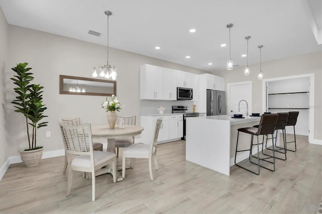 kitchen featuring sink, hanging light fixtures, an island with sink, stainless steel appliances, and white cabinets