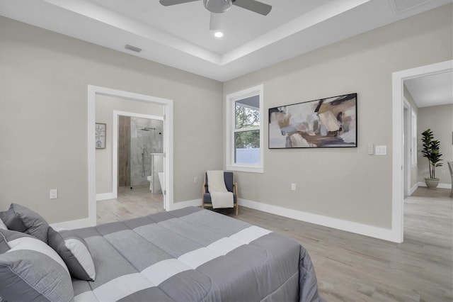 bedroom featuring light hardwood / wood-style flooring, a raised ceiling, ceiling fan, and ensuite bathroom