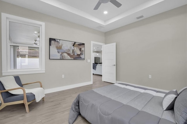 bedroom featuring ceiling fan, a tray ceiling, and light hardwood / wood-style floors