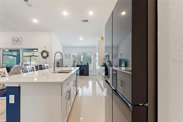 kitchen with sink, light tile patterned floors, a kitchen island with sink, light stone countertops, and white cabinets