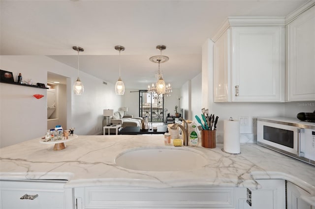 kitchen featuring light stone counters, sink, hanging light fixtures, and white cabinets