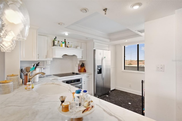 kitchen with white cabinetry, stainless steel appliances, a tray ceiling, and light stone countertops