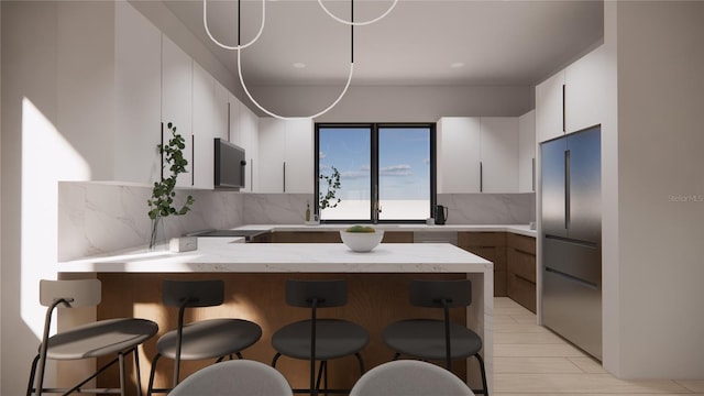 kitchen featuring a breakfast bar, stainless steel refrigerator, tasteful backsplash, white cabinets, and kitchen peninsula