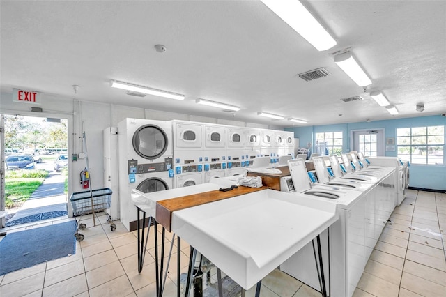 laundry area with stacked washer and dryer, light tile patterned floors, washing machine and dryer, and a textured ceiling