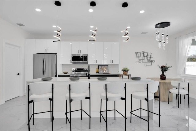 kitchen with white cabinetry, hanging light fixtures, a kitchen bar, and appliances with stainless steel finishes