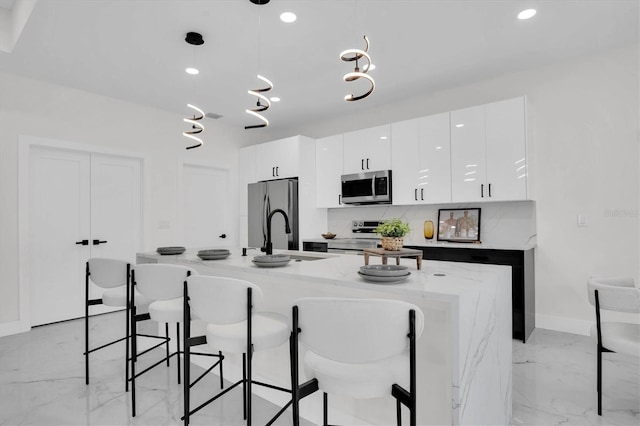 kitchen with sink, a kitchen island with sink, stainless steel appliances, white cabinets, and decorative light fixtures