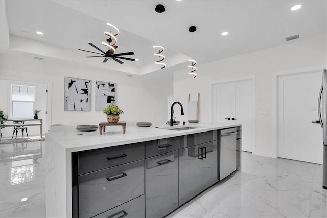 kitchen with decorative light fixtures, dishwasher, an island with sink, sink, and a tray ceiling