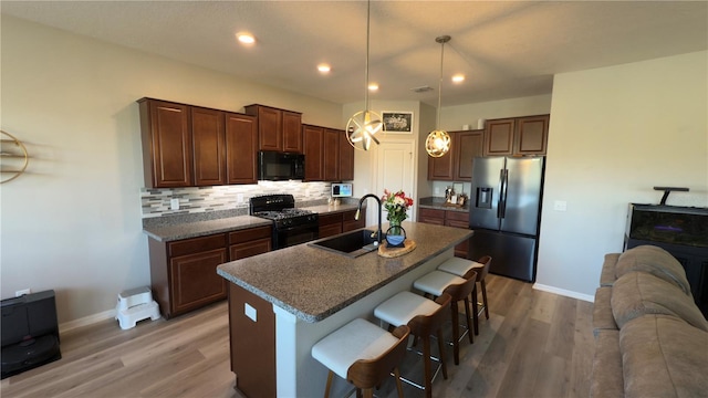 kitchen featuring pendant lighting, sink, a kitchen island with sink, black appliances, and a kitchen bar