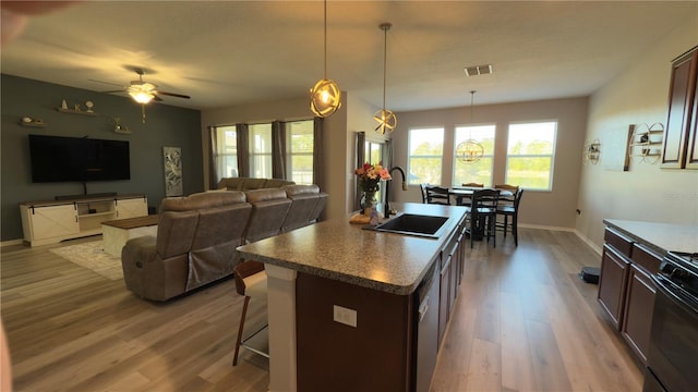 kitchen with pendant lighting, sink, a kitchen breakfast bar, a kitchen island with sink, and dark brown cabinetry