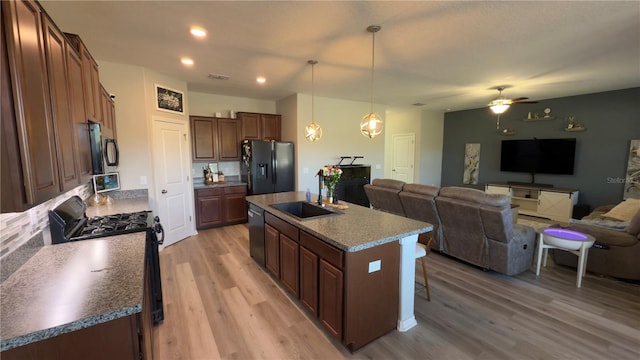 kitchen featuring decorative light fixtures, sink, a kitchen island with sink, black appliances, and light wood-type flooring