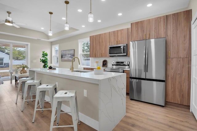 kitchen featuring appliances with stainless steel finishes, an island with sink, sink, a breakfast bar area, and hanging light fixtures