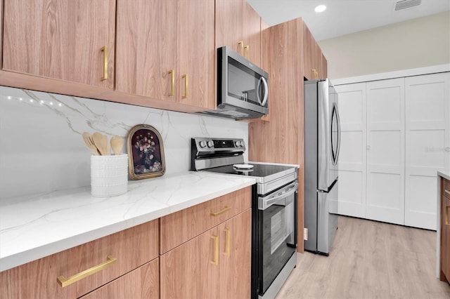 kitchen with stainless steel appliances, backsplash, light stone counters, and light hardwood / wood-style flooring