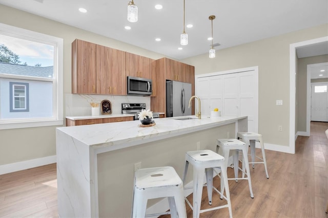 kitchen featuring a breakfast bar area, appliances with stainless steel finishes, light stone counters, a center island with sink, and decorative light fixtures