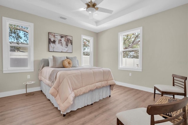 bedroom featuring ceiling fan, a raised ceiling, multiple windows, and light hardwood / wood-style flooring