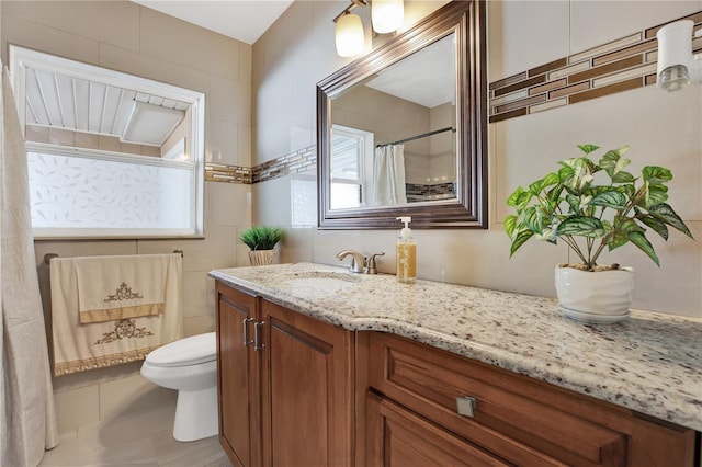 bathroom with tile patterned floors, vanity, toilet, and tile walls