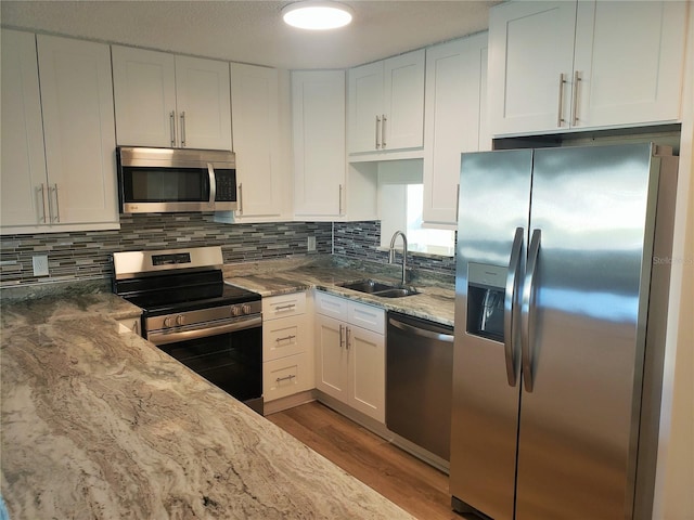 kitchen featuring sink, white cabinets, light hardwood / wood-style floors, stainless steel appliances, and light stone countertops