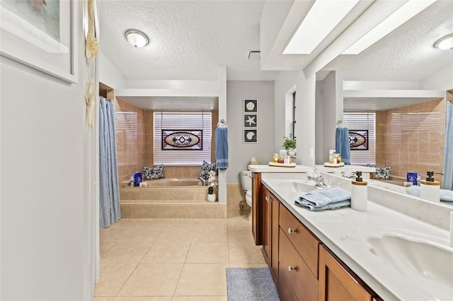 bathroom with tile patterned flooring, vanity, tiled bath, and a textured ceiling