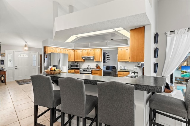 kitchen featuring a breakfast bar, light tile patterned floors, kitchen peninsula, stainless steel appliances, and a high ceiling