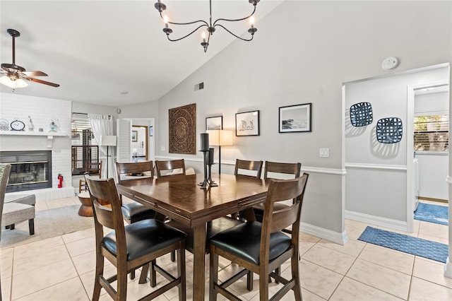 dining area with a brick fireplace, ceiling fan with notable chandelier, high vaulted ceiling, and light tile patterned flooring