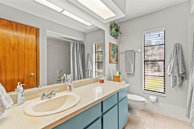 bathroom with tile patterned flooring, a skylight, a shower with shower curtain, vanity, and toilet