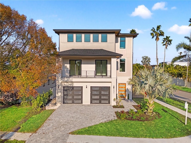 contemporary home with a front lawn, decorative driveway, an attached garage, and a balcony