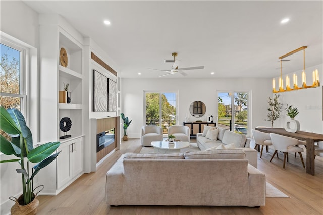 living room featuring built in shelves, ceiling fan with notable chandelier, and light wood-type flooring