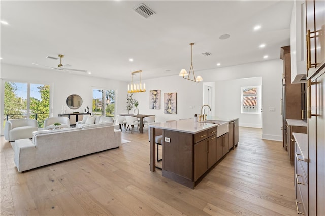 kitchen featuring recessed lighting, a sink, open floor plan, light wood finished floors, and a center island with sink